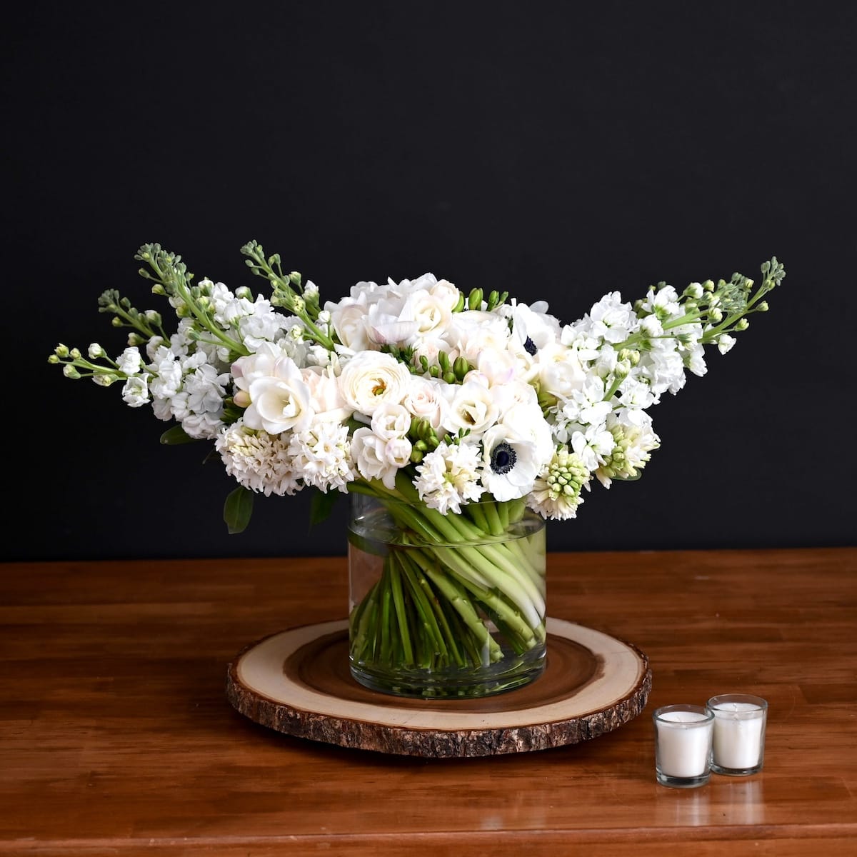 White anemones and blue hydrangea with delicate wildflowers in a hand-tied bouquet on a wooden surface