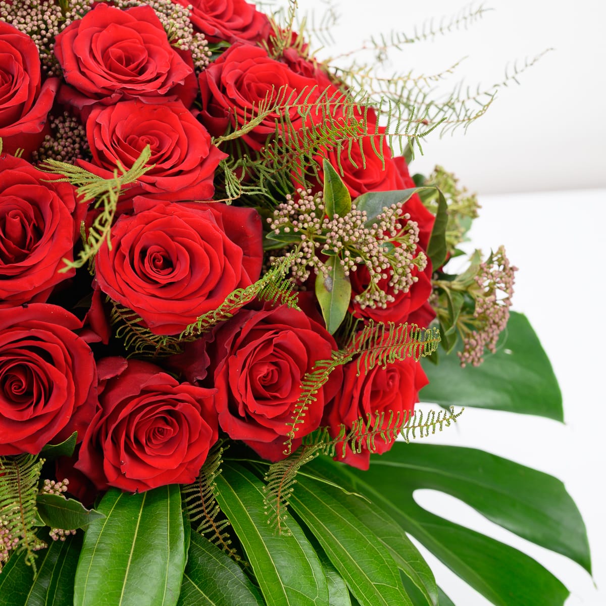 Close-up of deep crimson roses with golden fern fronds, sedum berry clusters and monstera leaf, romantic red rose arrangement Raleigh NC