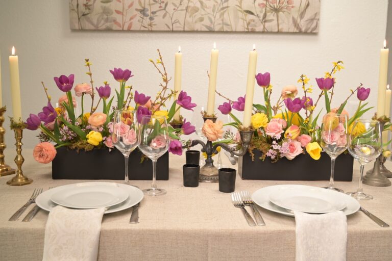 Warm peach and yellow table centerpieces with roses and tulips in small dark vessels at an elegant dinner setting