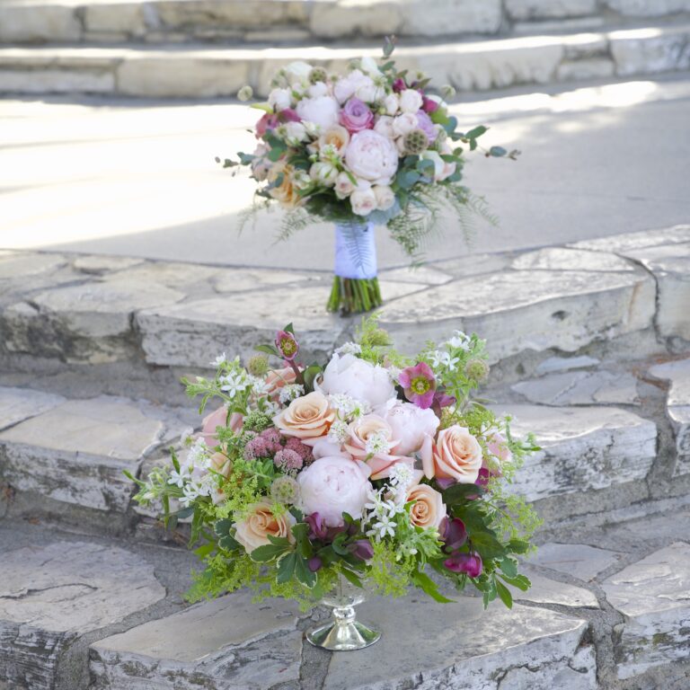 Pastel bridal bouquet with white roses, blue thistle and soft pink blooms against stone steps