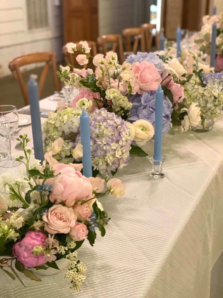 Long reception table with pink floral runner, taper candles and gold accents in a rustic barn venue