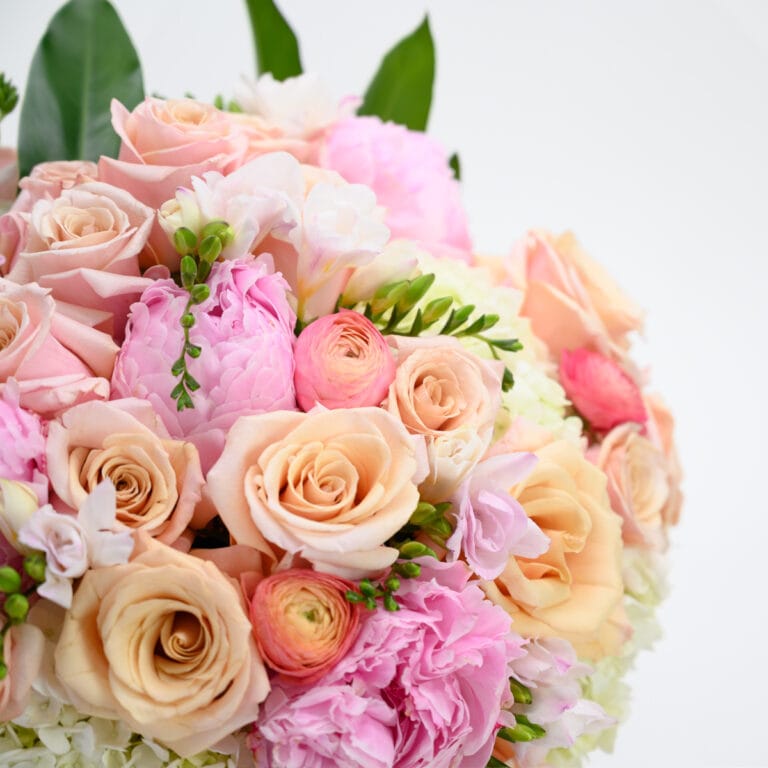 Close-up of peach roses, pink peonies and orange ranunculus with blush spray roses and white freesia in a lush dome arrangement, artisan flower delivery Raleigh NC