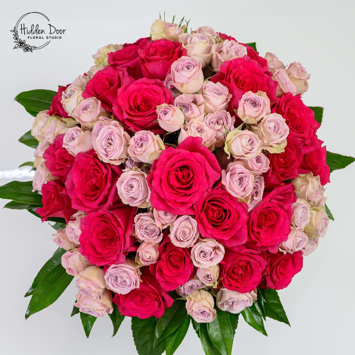 Vibrant pink and red roses arranged in a full rounded bouquet by Hidden Door Floral Studio