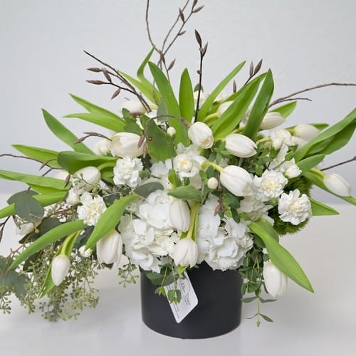 White lilies and soft greenery in a simple glass vase suitable for hospital flower delivery in the Raleigh Triangle area - hospital flowers