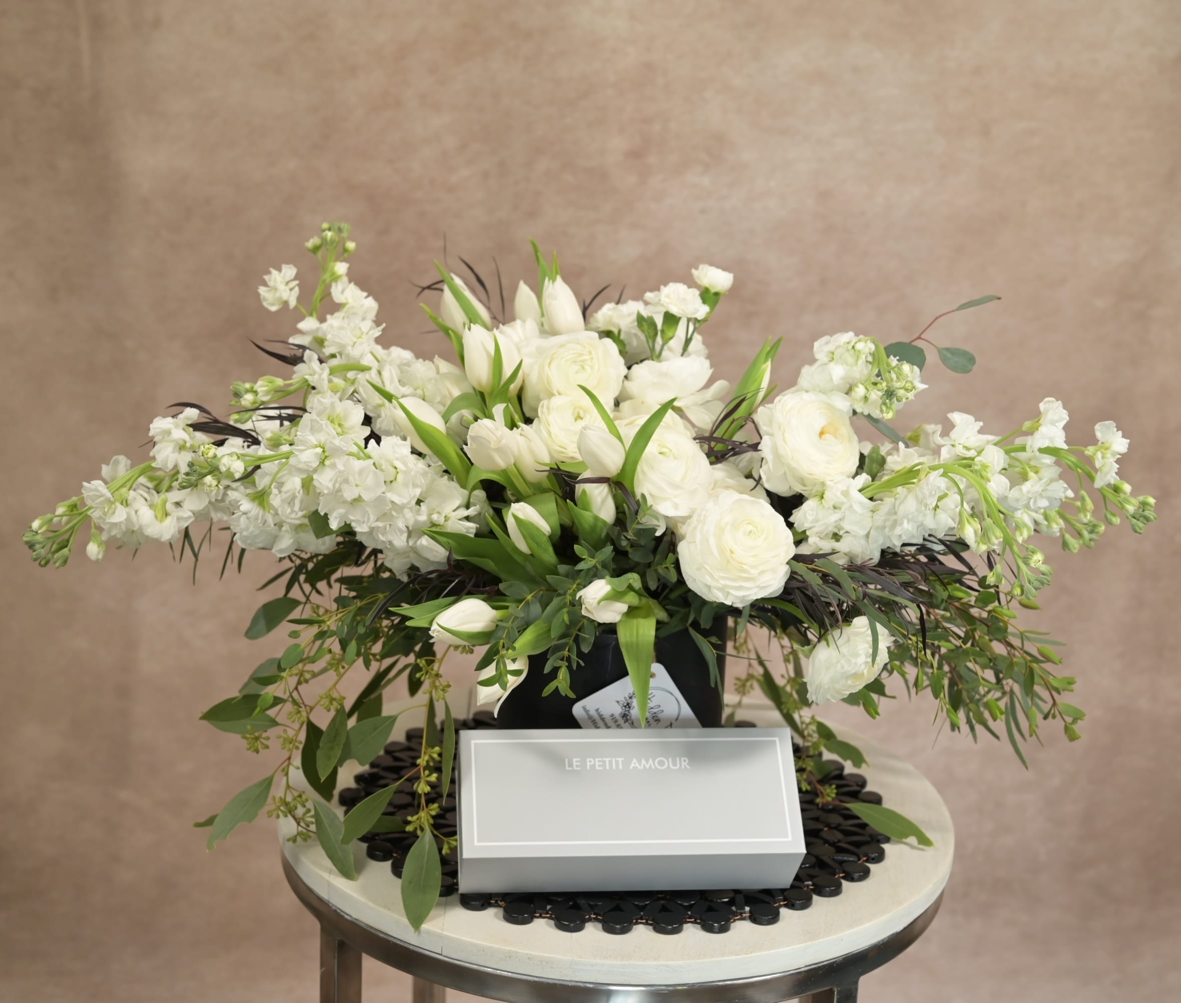 Grand white arrangement with lilies, lisianthus, roses and stock accented by dark purple foliage