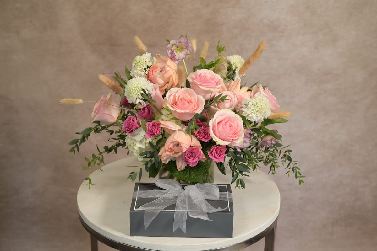 Pink roses and blush stock with white blooms and dark decorative branches in a clear glass vase